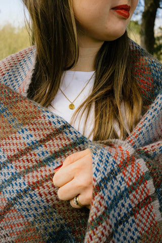 A cozy large checked random recycled wool blanket in multicolored plaid draped over a person’s shoulders