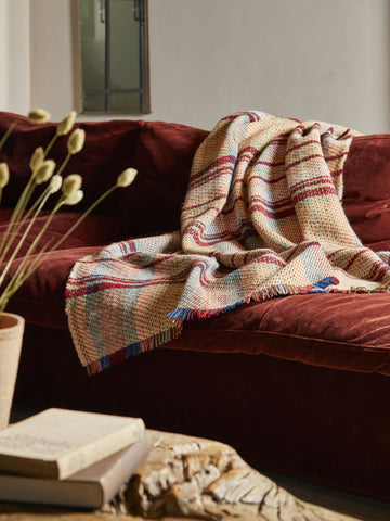 A cozy large checked random recycled wool blanket in soft beige with muted red blue and green stripes and multicolored fringe