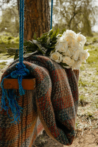 A cozy multicolored checked random recycled wool blanket draped over a wooden swing with blue rope suspenders