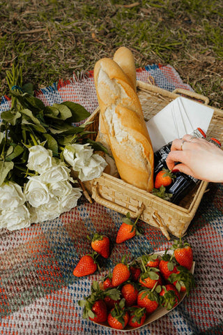 Large checked random recycled wool blanket next to golden-brown baguette and fresh strawberries with white roses