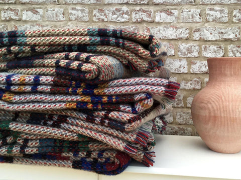 Stack of multicolored large checked random recycled wool blankets with fringed edges made from soft recycled wool