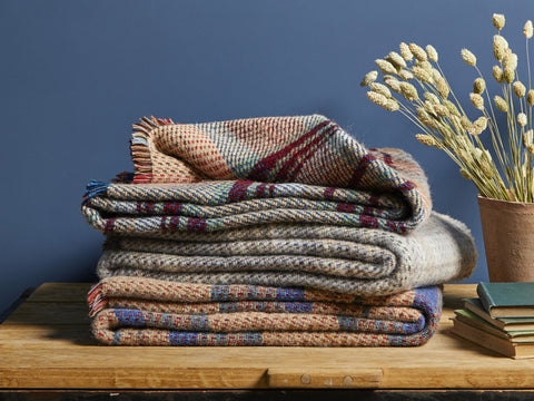 Stack of cozy large checked random recycled wool blankets in earthy tones with textured plaid patterns