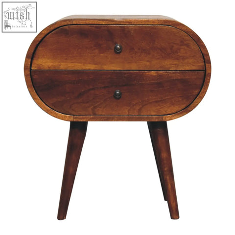 A large chestnut circular bedside table with sleek oval shape, two drawers, and tapered wooden legs