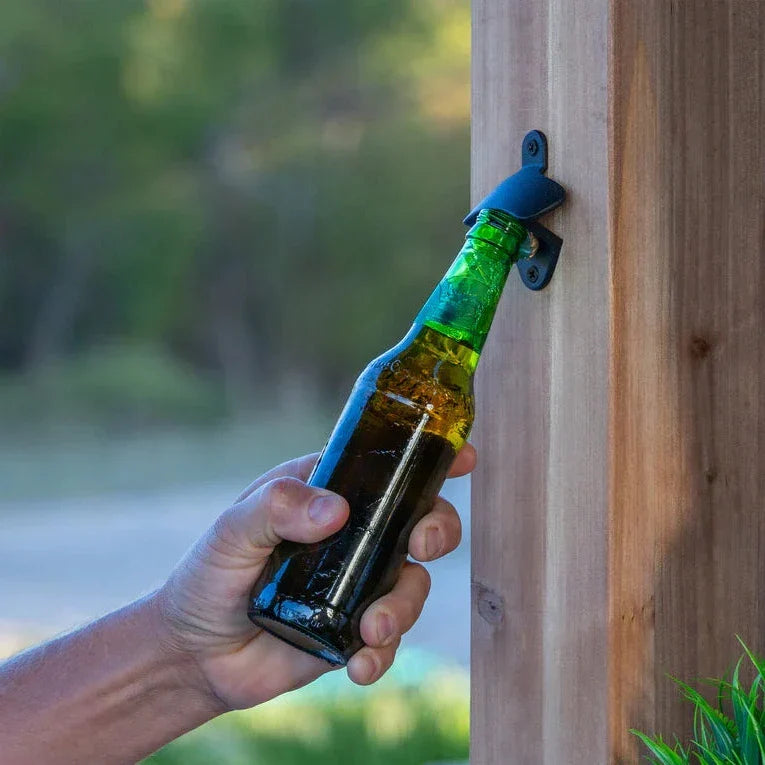 Black metal bottle opener gripping green beer bottle on large rustic wooden bar shelving unit for garden bar setup