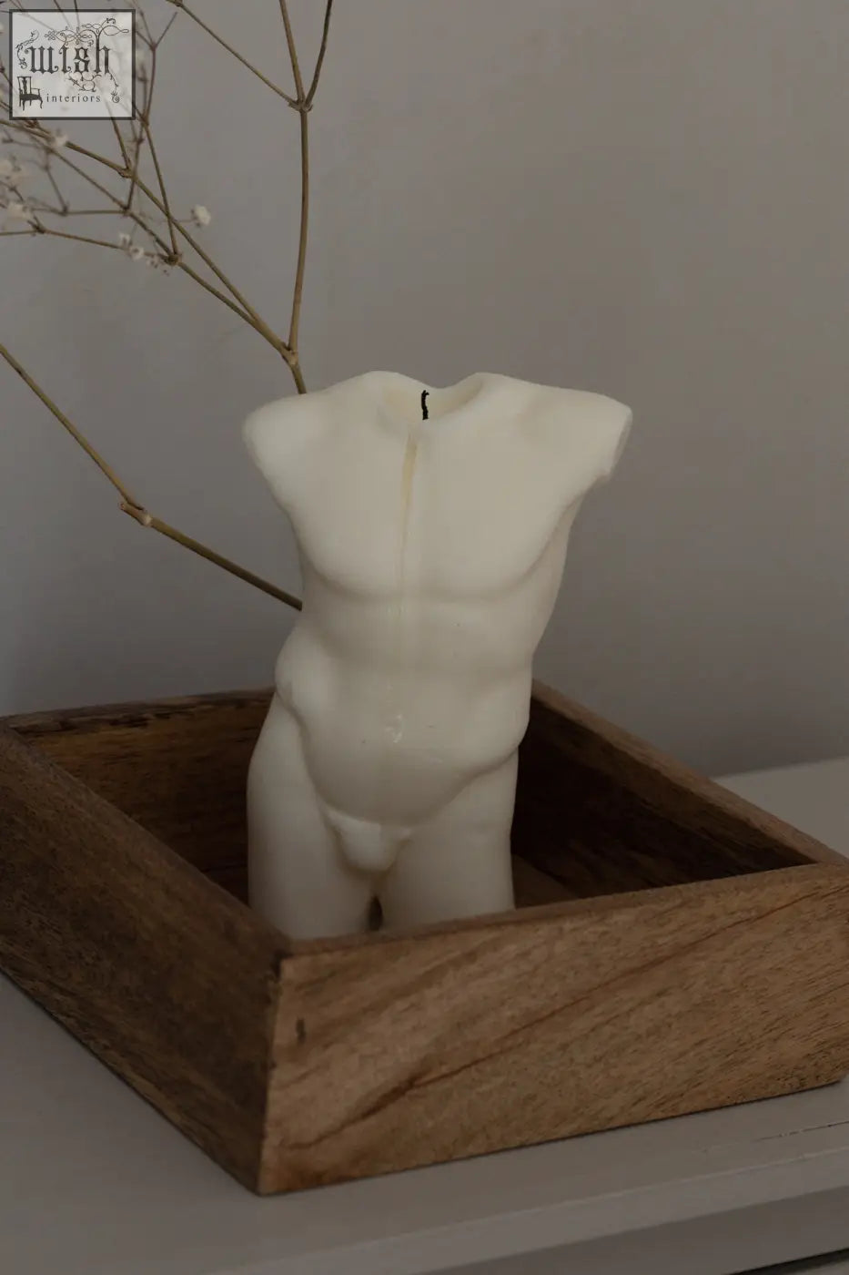 A white male bust candle shaped like a david torso with defined abs sitting in a wooden box
