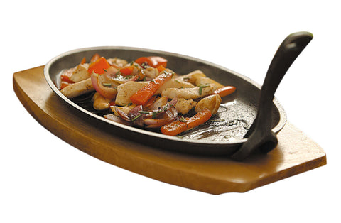 Large black cast iron sizzler dish with lifting handle holding sautéed chicken and vegetables