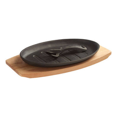 Black oval cast iron sizzler dish with built-in lifting handle resting on wooden serving board