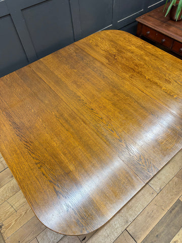 A large solid oak gateleg dining table with warm amber finish and smooth rounded edges showing wood grain