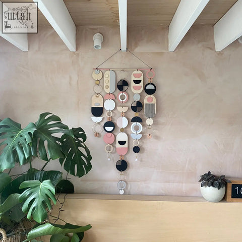 Large wall art featuring modern geometric hand painted wooden and metal shapes in pastel pink black white and beige tones