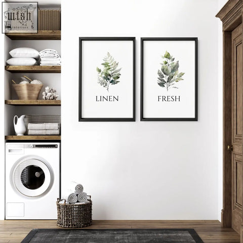 Two framed laundry room art prints with green watercolor leaves and black text linen and fresh in black frames