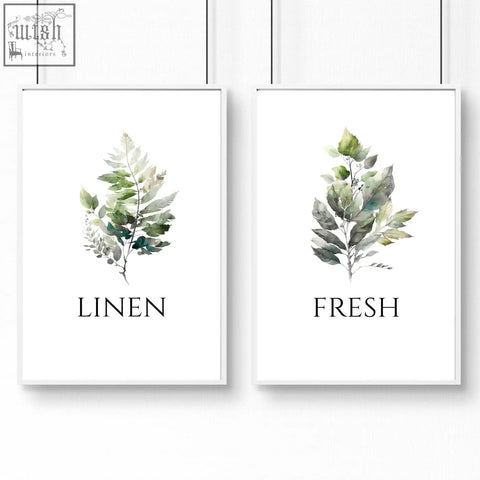 Two framed laundry room art prints featuring watercolor leaf illustrations in soft green and gray tones with white frames