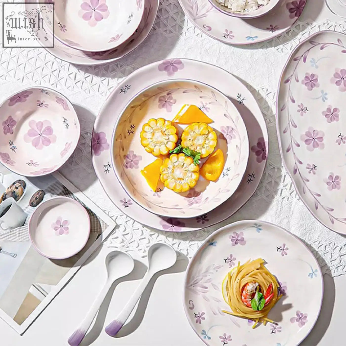 A delicate white ceramic layla orchid dining set with pink blue floral patterns and a bowl of grilled corn on the cob