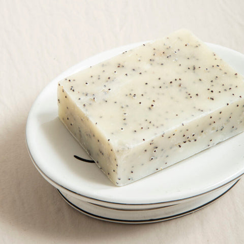 A rectangular off-white bar soap with black poppy seed specks on a le bain white ceramic soap dish