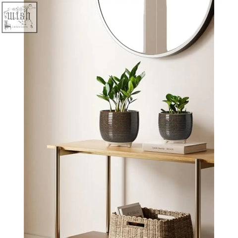 Two dark gray ribbed ceramic plant pots with white feet sit on a wooden table for indoor plants and office use