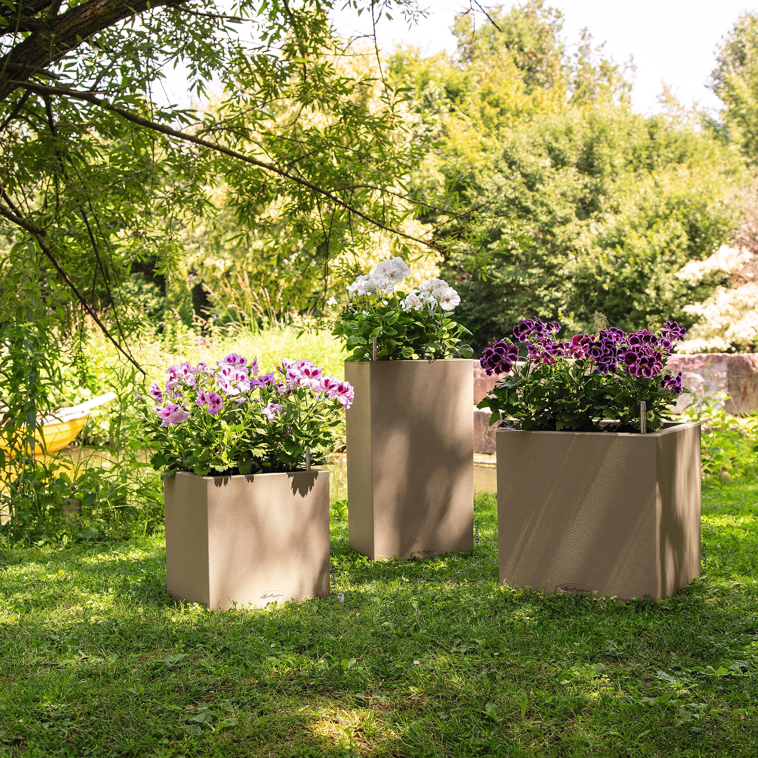 Three taupe plastic watering plant pots canto stone 30 with textured surface on grass under trees