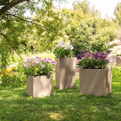 Three taupe plastic watering plant pots canto stone 30 with textured surface on grass under trees