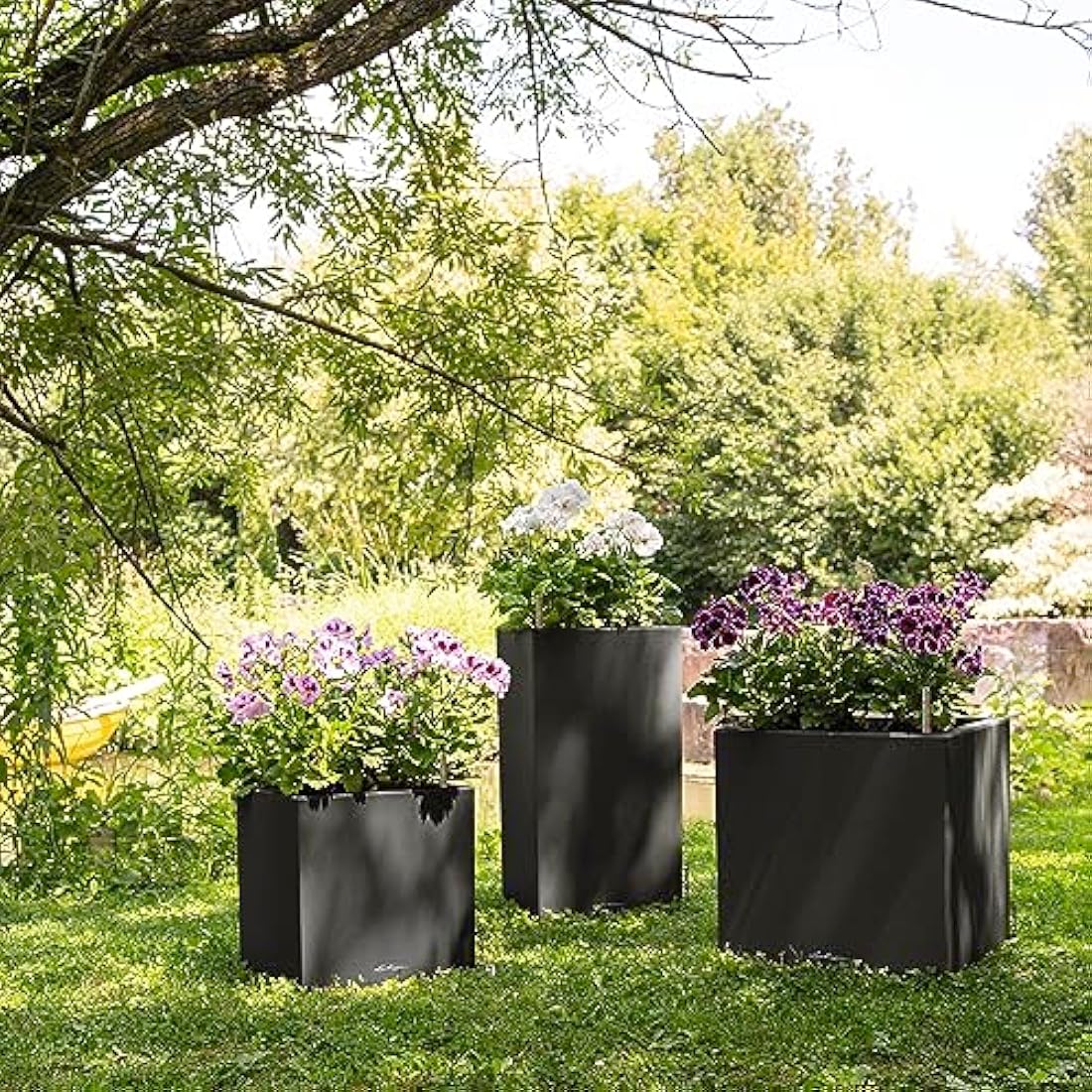 Three sleek graphite black lechuza self watering plant pots with water reservoir filled with purple white flowers