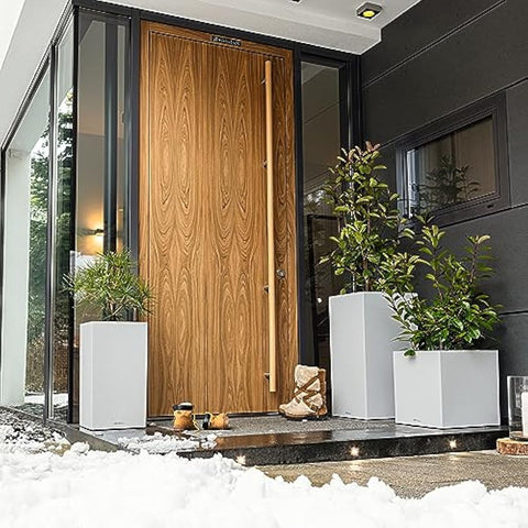 A modern wooden front door next to a canto stone grey self watering plant pot with drainage hole