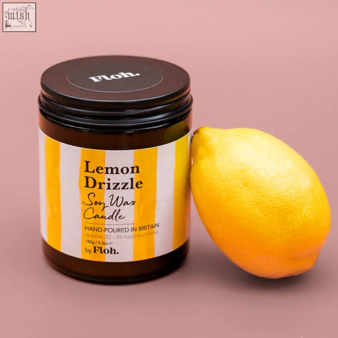 A vibrant yellow lemon sits beside a lemon drizzle soy wax candle by floh made from natural vegetable soy wax