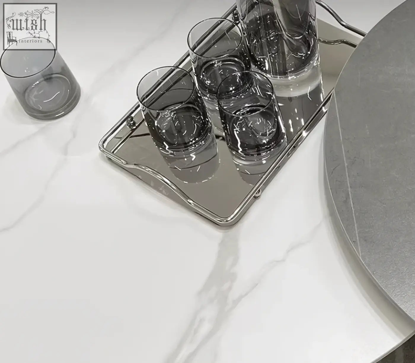 Silver mirrored tray with four dark gray glass tumblers and a pitcher on leonor nesting coffee table with steel base