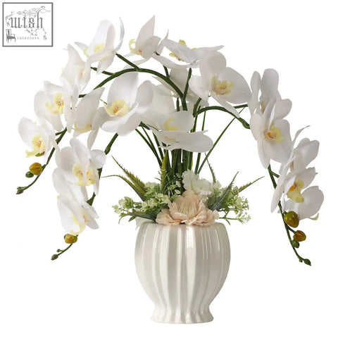 White ceramic vase with vertical ridges holds lesing artificial flowers ochids for indoor home decoration