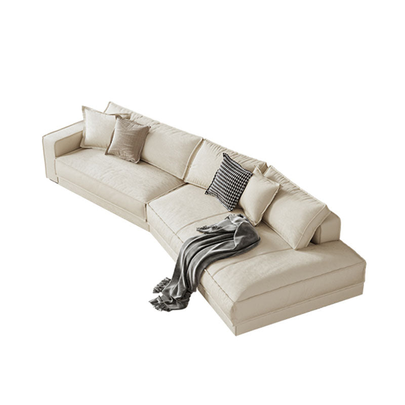 Beige lester curved seater sofa with plush cushions and gray throw blanket draped over the corner