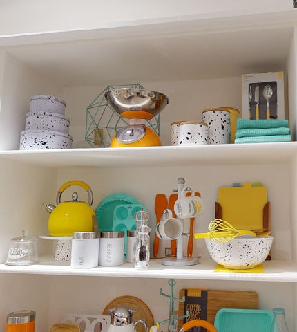 Yellow enamel tea kettle with satin stainless steel handle and spout sitting on white shelf in liberty enamel set