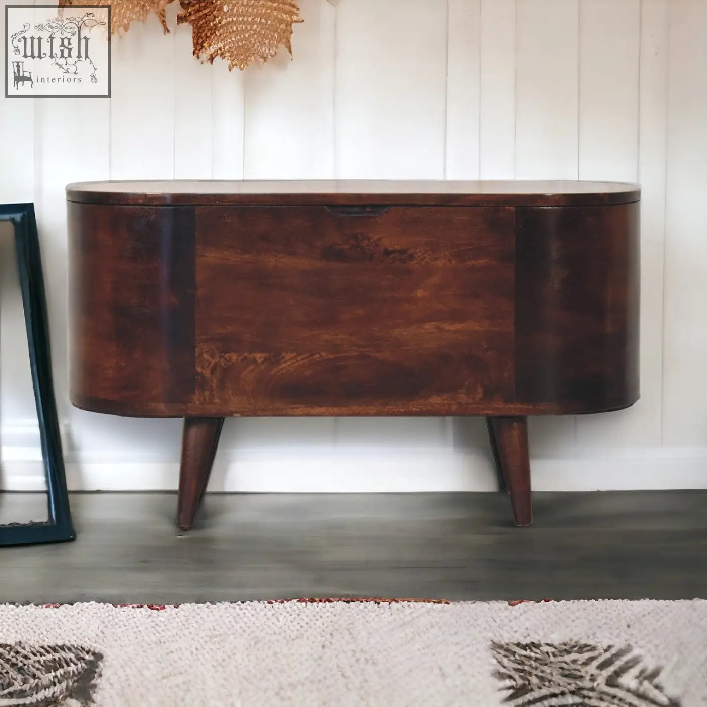 Dark brown wooden sideboard with curved top and tapered legs next to a light walnut rounded lid-up blanket box storage bench