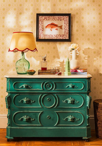 Teal-green antique-style wooden dresser with ornate carved drawers and decorative handles in minimalist style