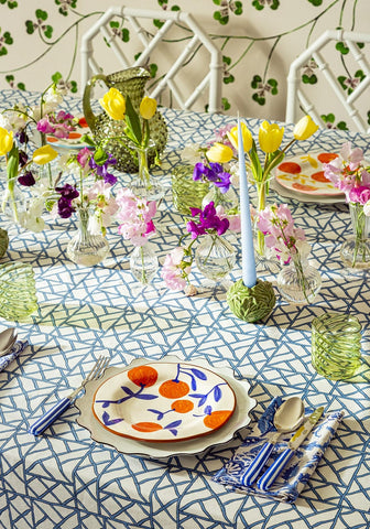 A white ceramic plate with scalloped edge and orange blue botanical design on lily’s blue bamboo breeze tablecloth