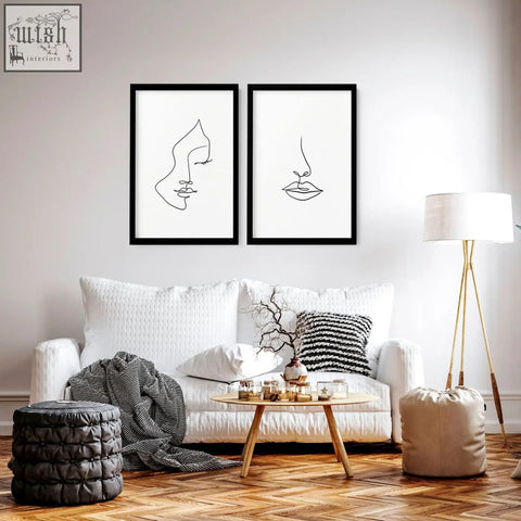Two minimalist black-framed line art wall art prints with abstract faces hang above a white sofa in a living room