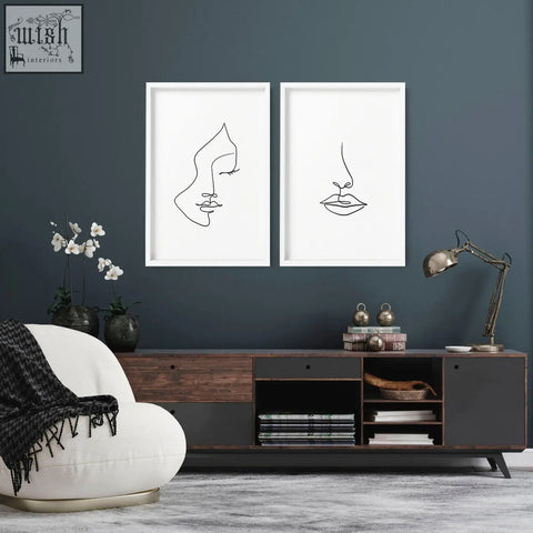 Two minimalist black line art wall art prints in white frames showing a face and lips on a dark blue living room wall