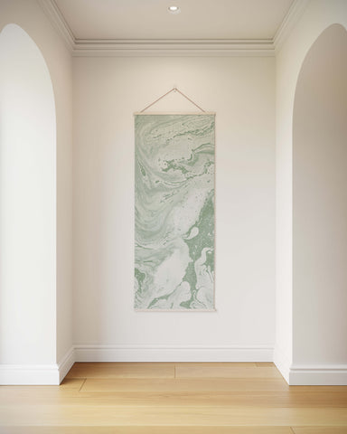 A vertical liquid marble tapestry wall hanging with soft green and white marbled pattern suspended by a wire hanger
