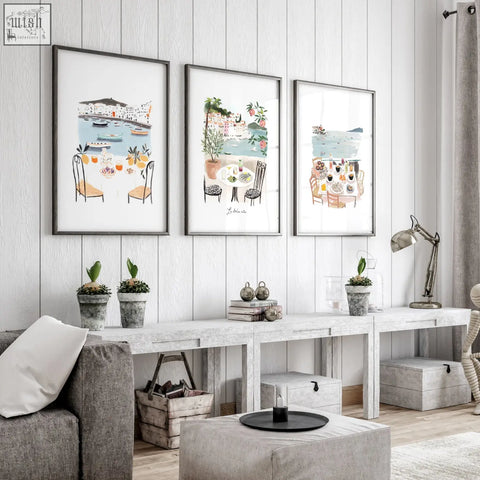 Three framed mediterranean coastal living room artwork illustrations of tables chairs and food on a white wooden wall