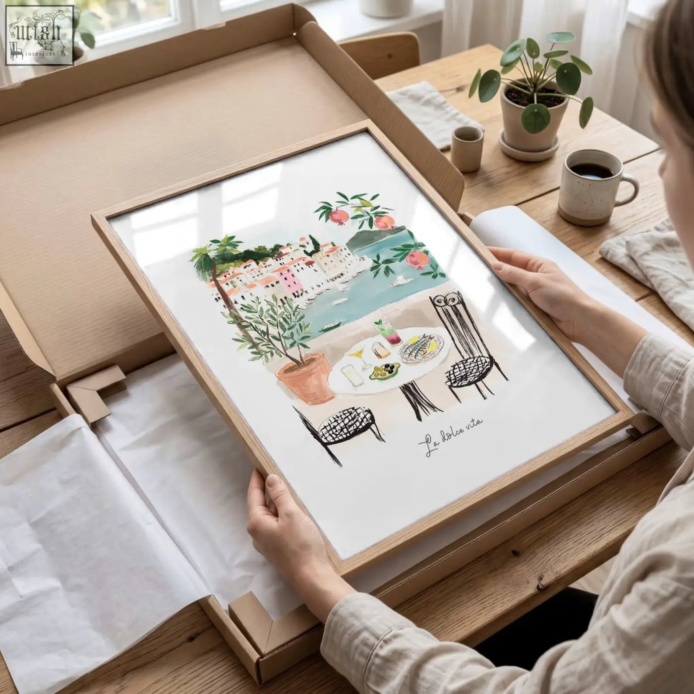 A framed watercolor living room artwork featuring a mediterranean coastal café scene in soft pastel tones
