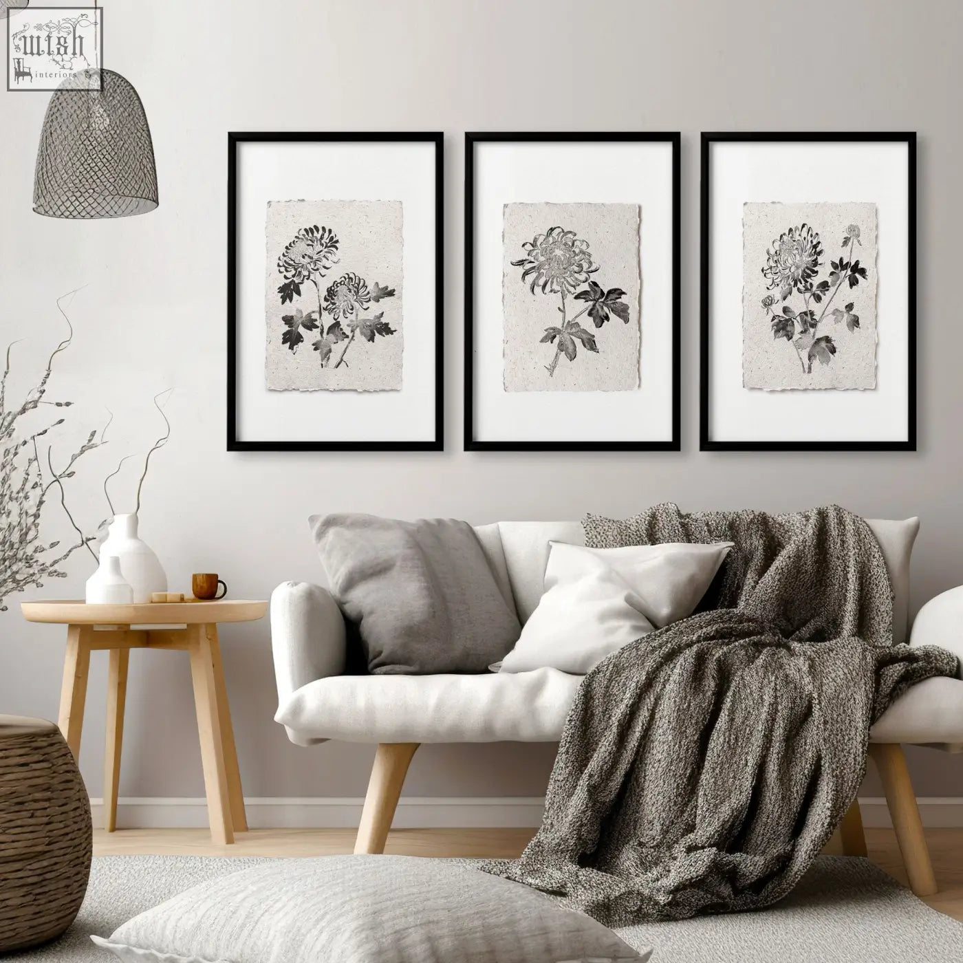 Three black-framed living room prints of botanical chrysanthemum art on textured beige paper above white sofa