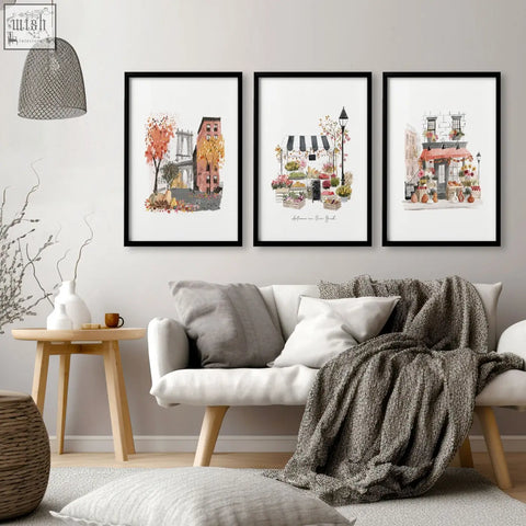 Three framed watercolor autumn in new york cityscape prints with black frames hang on the living room wall above a sofa