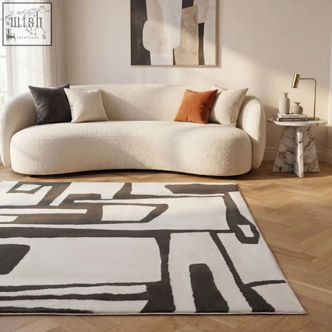 Modern cream-colored plush sofa with curved design and black white orange pillows on loft abstract dark grey rug