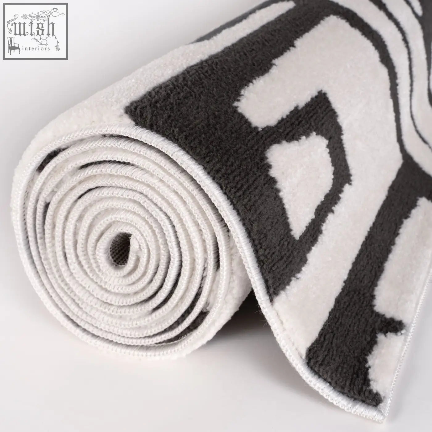 A plush rolled-up loft abstract dark grey rug with bold black and white geometric pattern on soft terry cloth