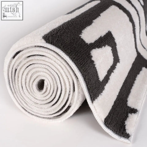 A plush rolled-up loft abstract dark grey rug with bold black and white geometric pattern on soft terry cloth