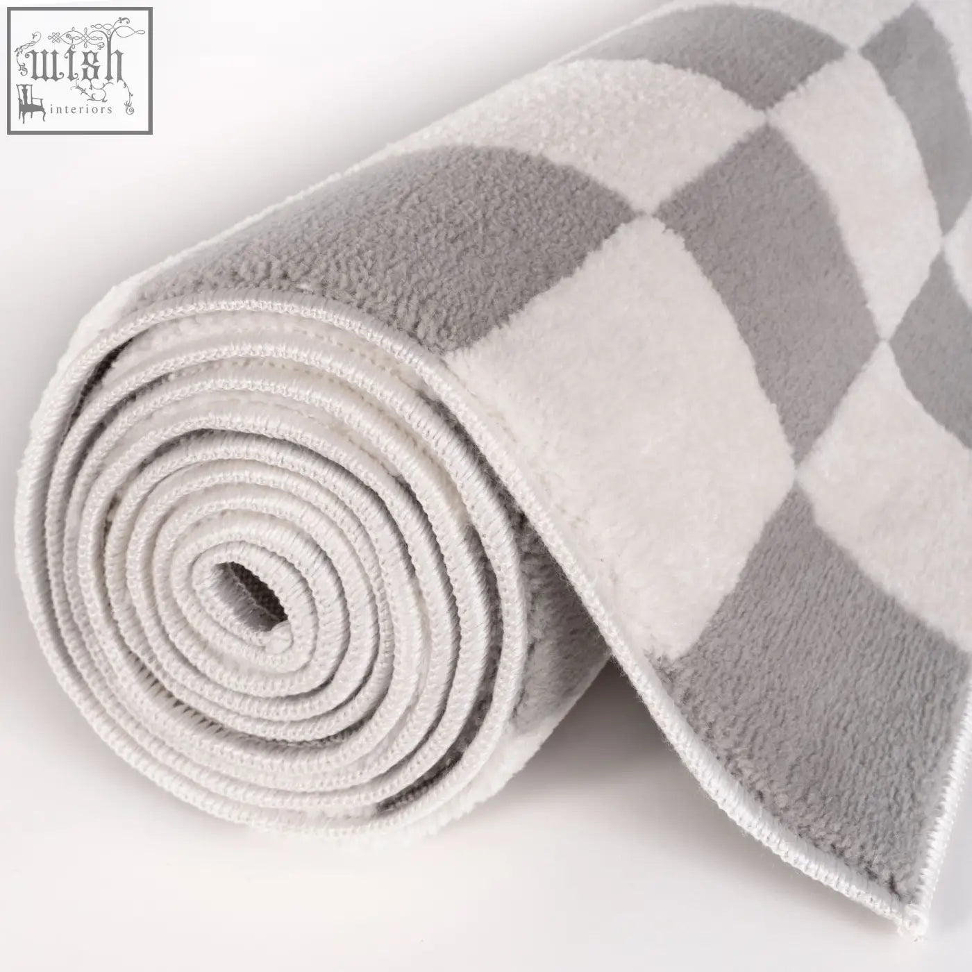 A plush rolled-up bath towel with a soft grey and white checkered pattern next to a loft checkerboard grey rug
