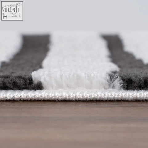 A plush dark grey rug with white and grey stripes and a soft textured surface perfect for cozy spaces