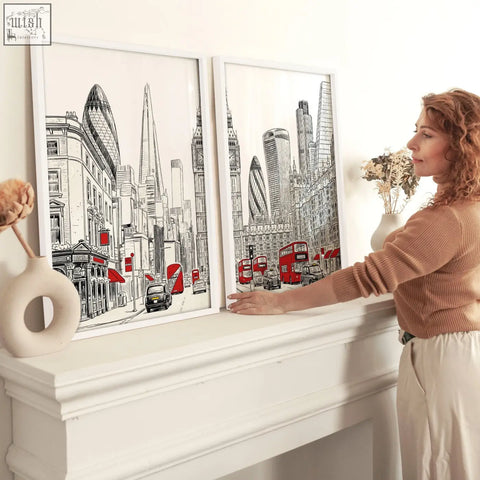 Two framed london abstract art prints featuring black white red city skyline with buses and taxis on a mantelpiece
