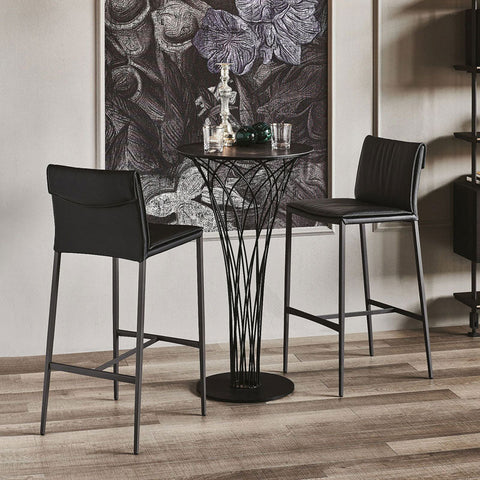 Lorelei bar stool set with black leather seats and sleek metal frames paired with a black wrought iron pedestal table