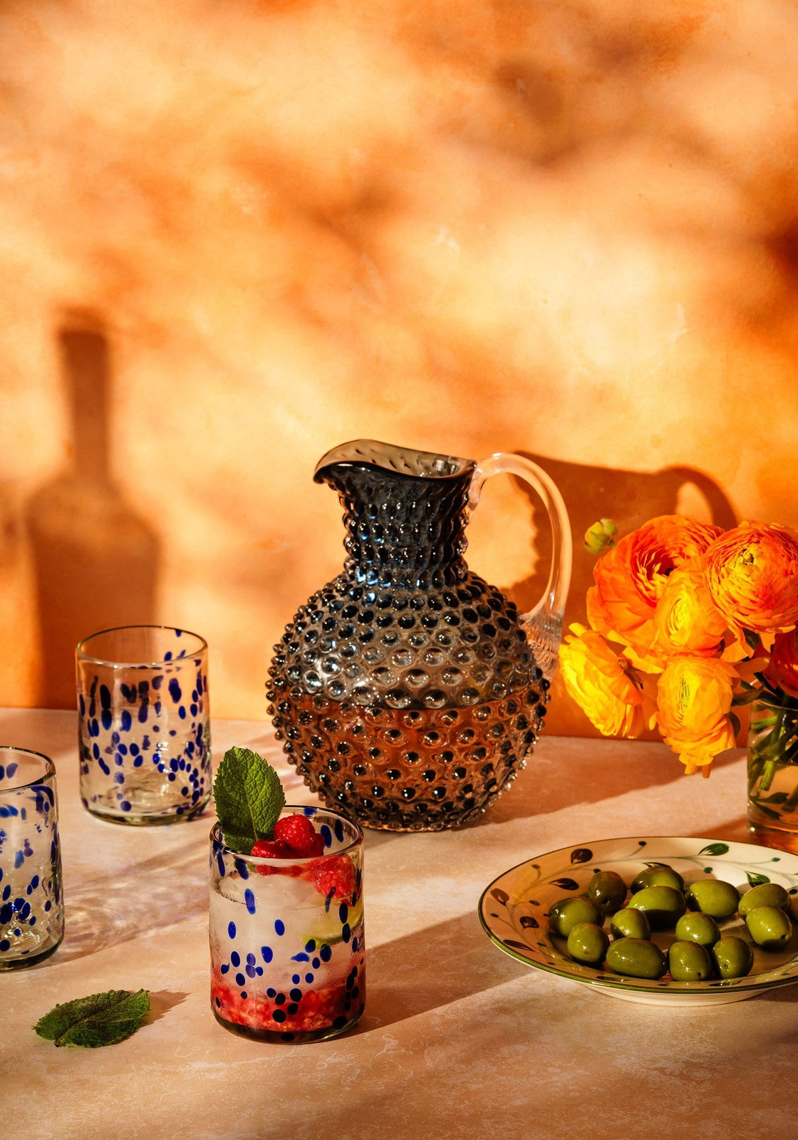 A dark blue louisa confetti tumbler glass pitcher with hobnail texture and clear handle, perfect for serving drinks