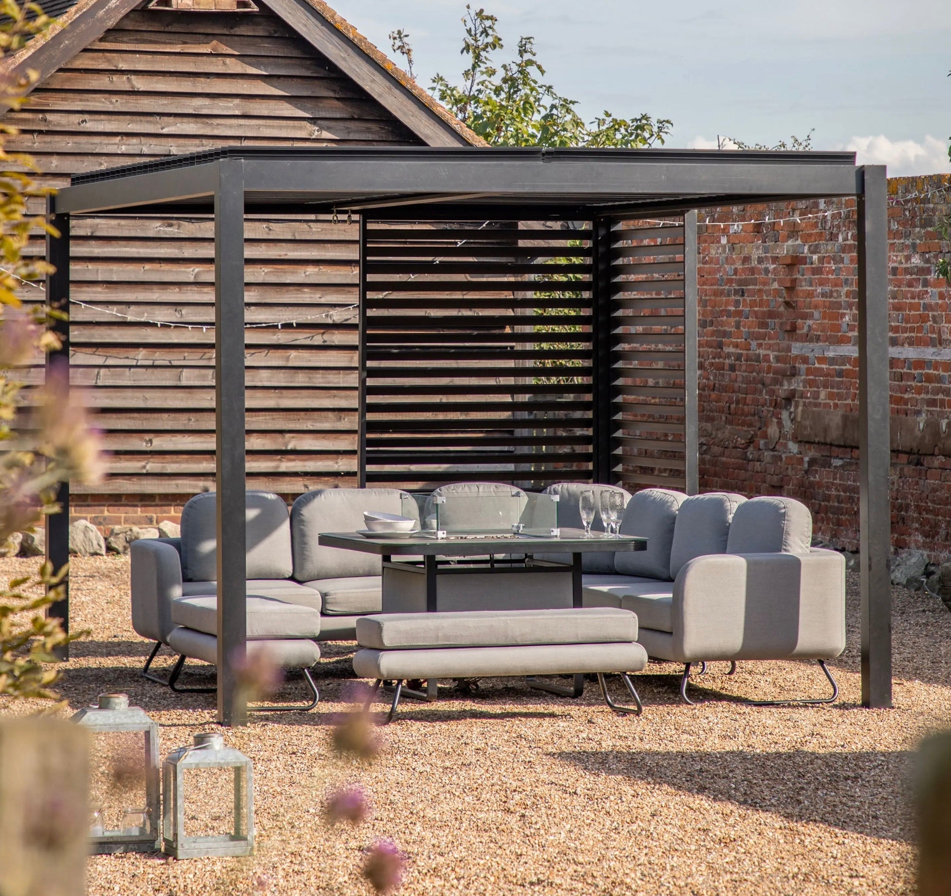 Modern gray outdoor sectional sofa set with metal frame and matching bench under a black louvre side panel pergola