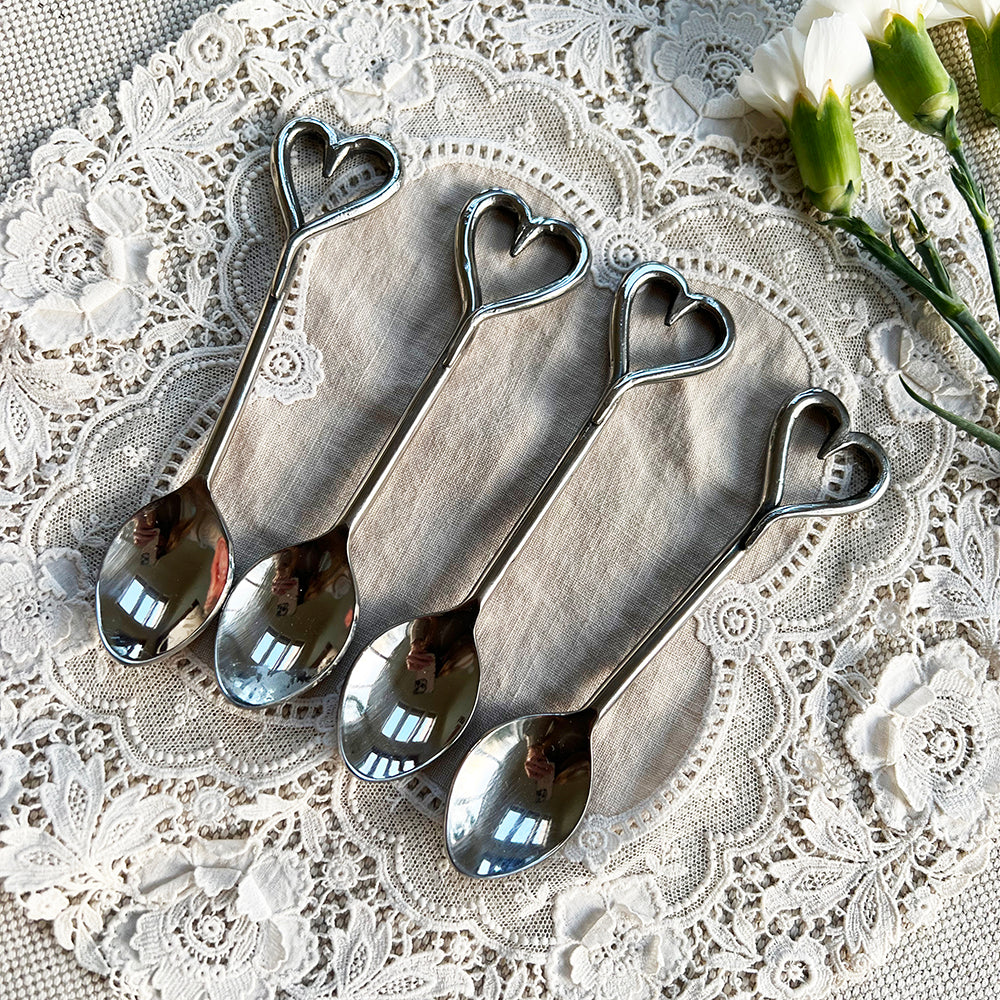 Four shiny silver love heart spoons arranged on a lace doily perfect for romantic table settings