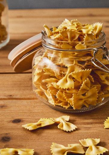A luca square 800ml glass jar with wooden lid and metal clasp filled with golden bow-tie pasta
