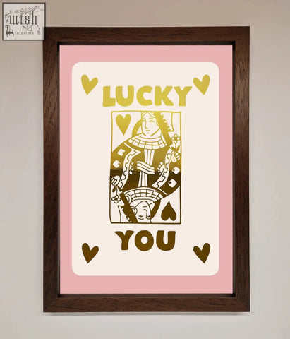 A lucky you foil print of a gold queen of spades playing card in cream with pink border in a dark wood frame with fast shipping times