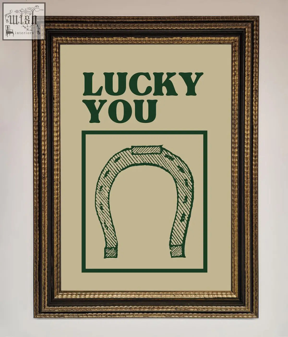 A framed wall art print featuring a green horseshoe and lucky you text on an off-white background